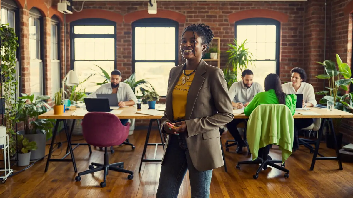 A founder laughing in a bright brick loft, three teammates working at desks behind her
